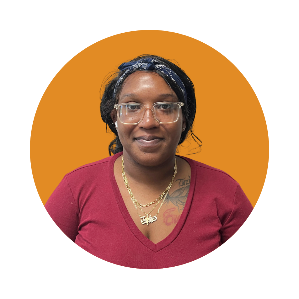 Ms. Jahlyn, Behavior Technician at Therapy Smarts, wearing a maroon shirt and glasses, with a gold necklace, against a vibrant orange background.